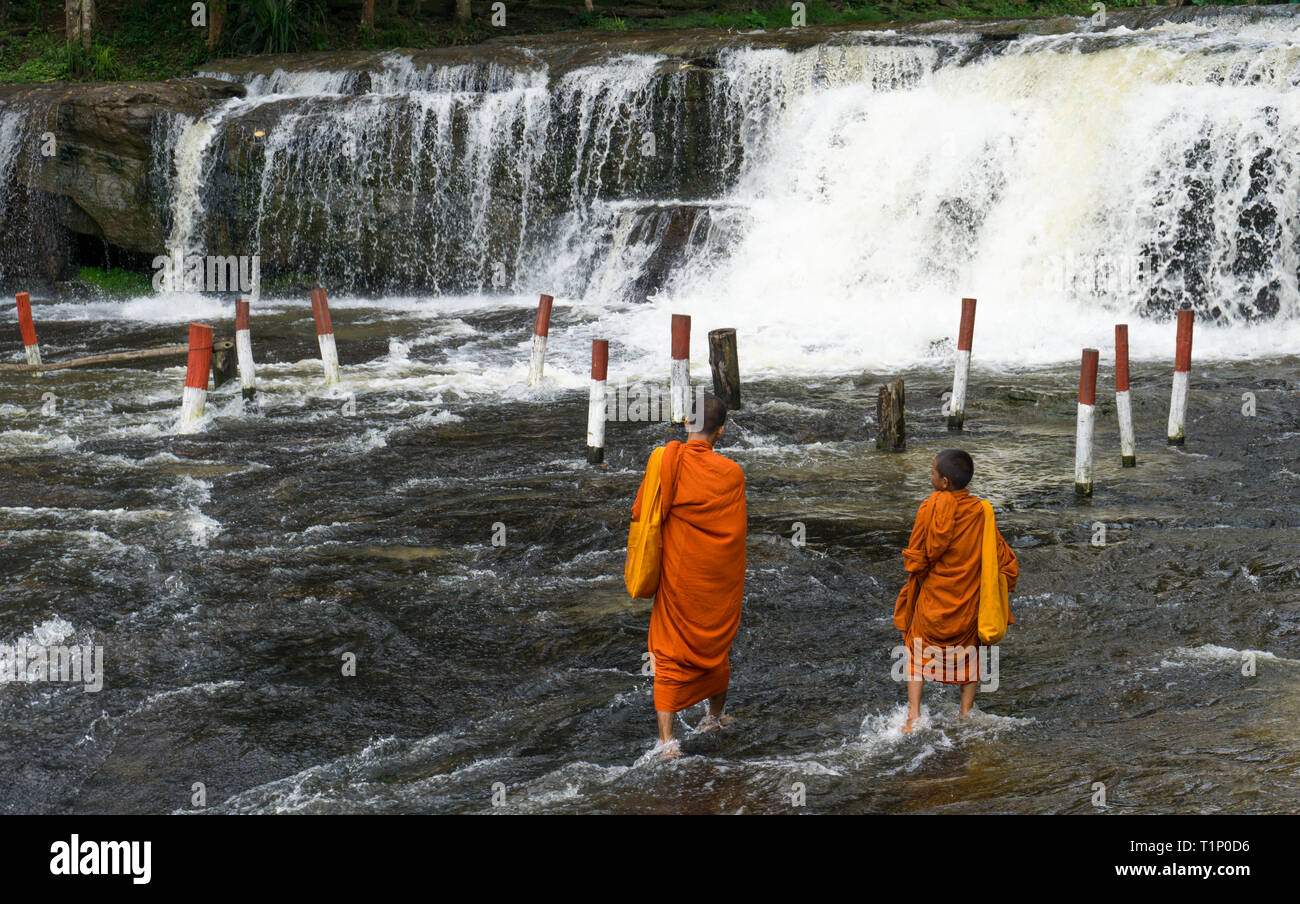 Zwei junge buddhistische Mönche wandern durch seichtes Wasser in Richtung Wasserfall Stockfoto