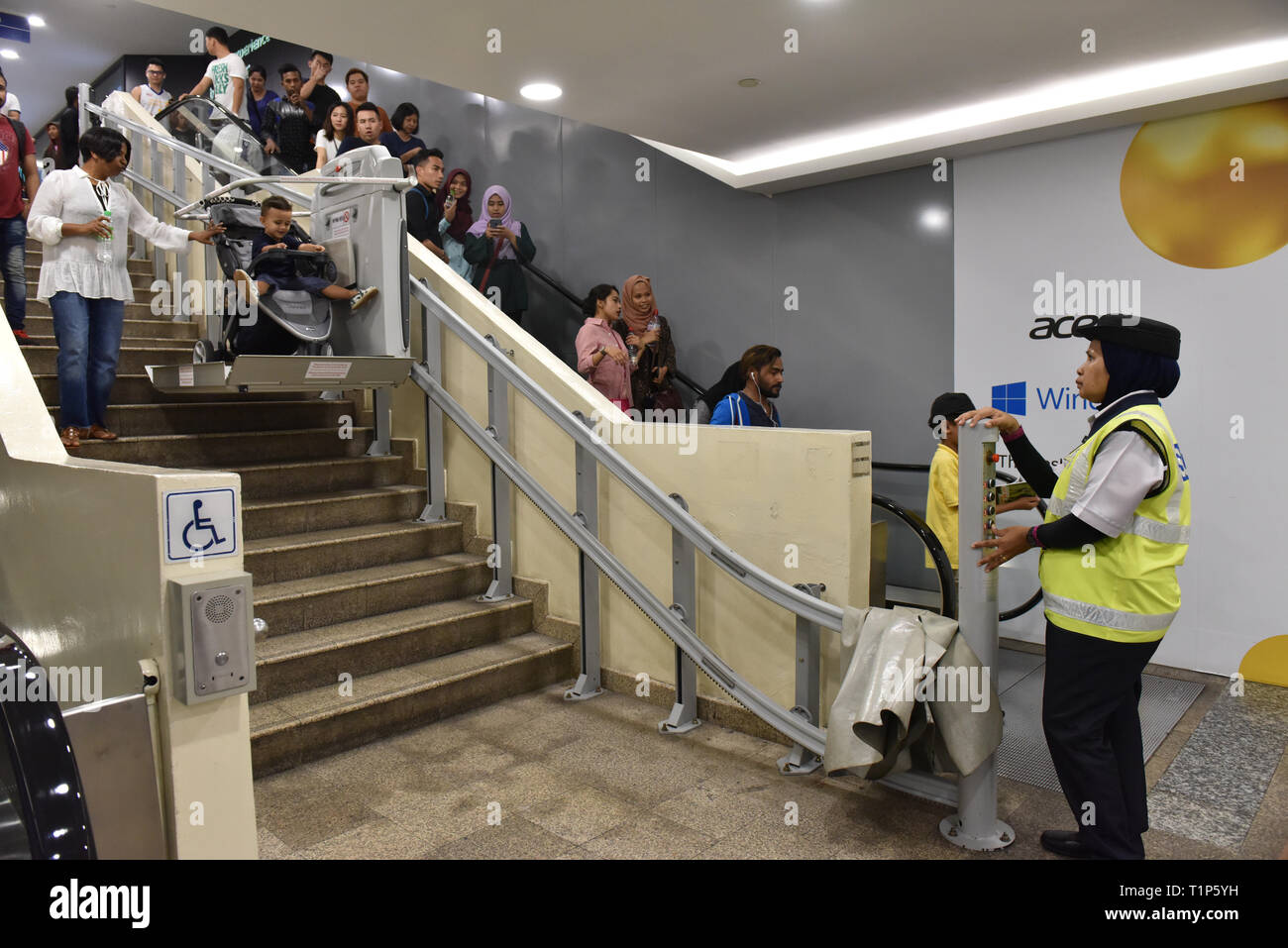 Muslimische Polizistin helfen, eine Mutter und ihr Baby die Treppen hinunter in der U-Bahn mit einer elektrisch betätigten Stuhl, Kuala Lumpur Stockfoto