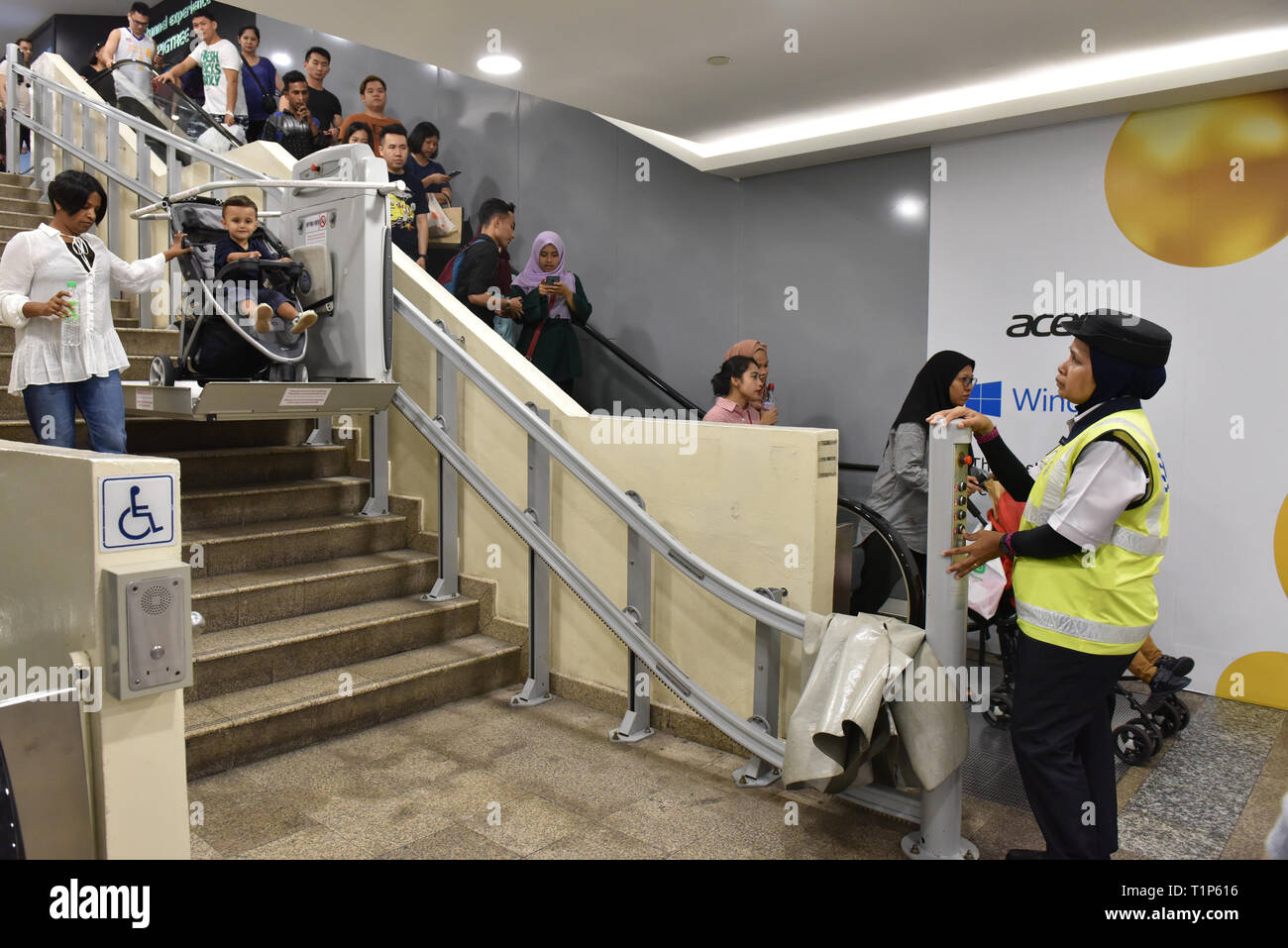 Muslimische Polizistin helfen, eine Mutter und ihr Baby die Treppen hinunter in der U-Bahn mit einer elektrisch betätigten Stuhl, Kuala Lumpur Stockfoto