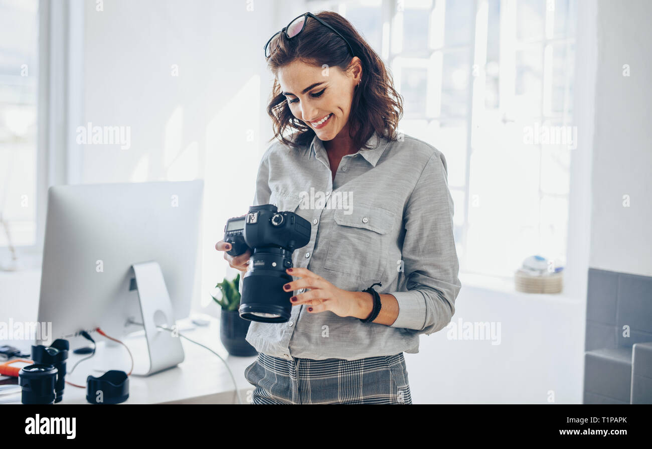 Fotografin Kontrolle Bilder auf Kamera und lächelnd. Kaukasische Frau in Casuals stehen in ihrem Büro mit Blick auf die Fotos auf ihrem DSLR-Kameras Stockfoto