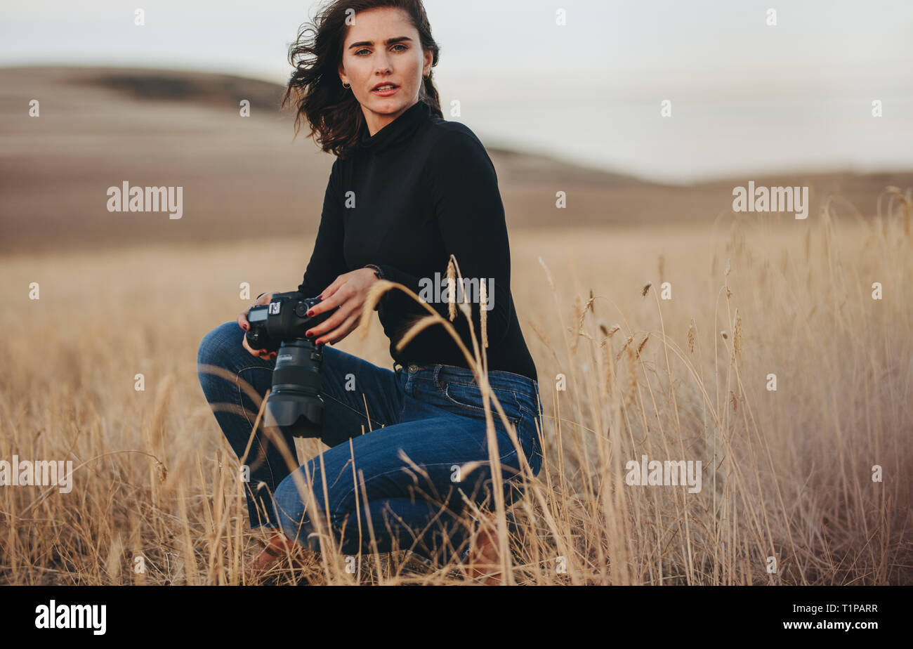 Professionellen Fotografen auf ein Fotoshooting im Freien. Junge Frau mit einem Foto Kamera hocken in trockenem Gras im freien Feld. Stockfoto