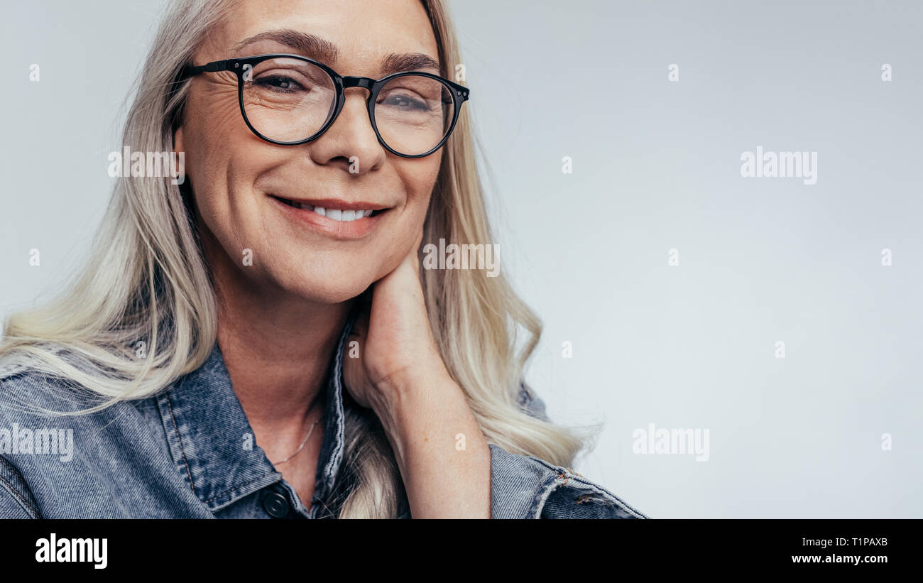 Entspannt senior kaukasischen Frauen mit Brille mit Kamera suchen und lächelnd. Positive senior Frau gegen grauen Hintergrund. Stockfoto
