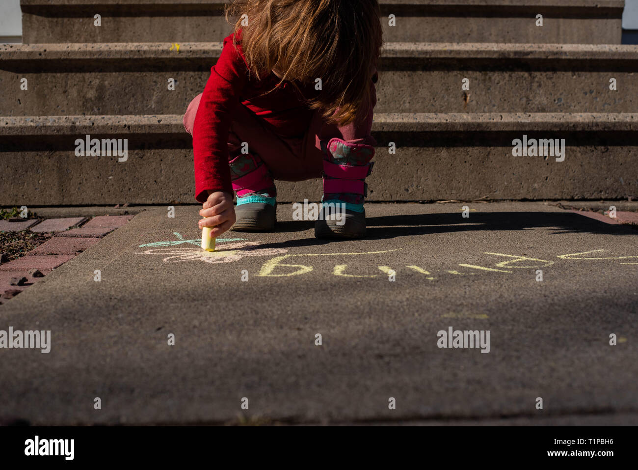 Auf ein 4-jähriges Mädchen Holding sidewalk Chalk auf einem Bürgersteig im Frühjahr. Stockfoto