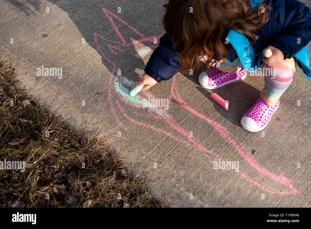 Auf ein 4-jähriges Mädchen Holding sidewalk Chalk auf einem Bürgersteig im Frühjahr. Stockfoto