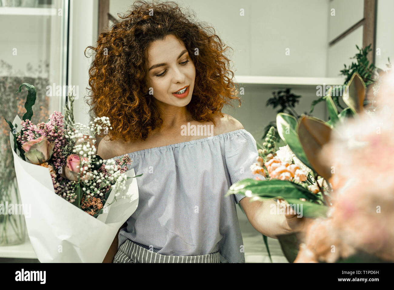 Curly blauäugigen Florist lächelnd während Sitzung Klienten in ihrem Blumengeschäft Stockfoto