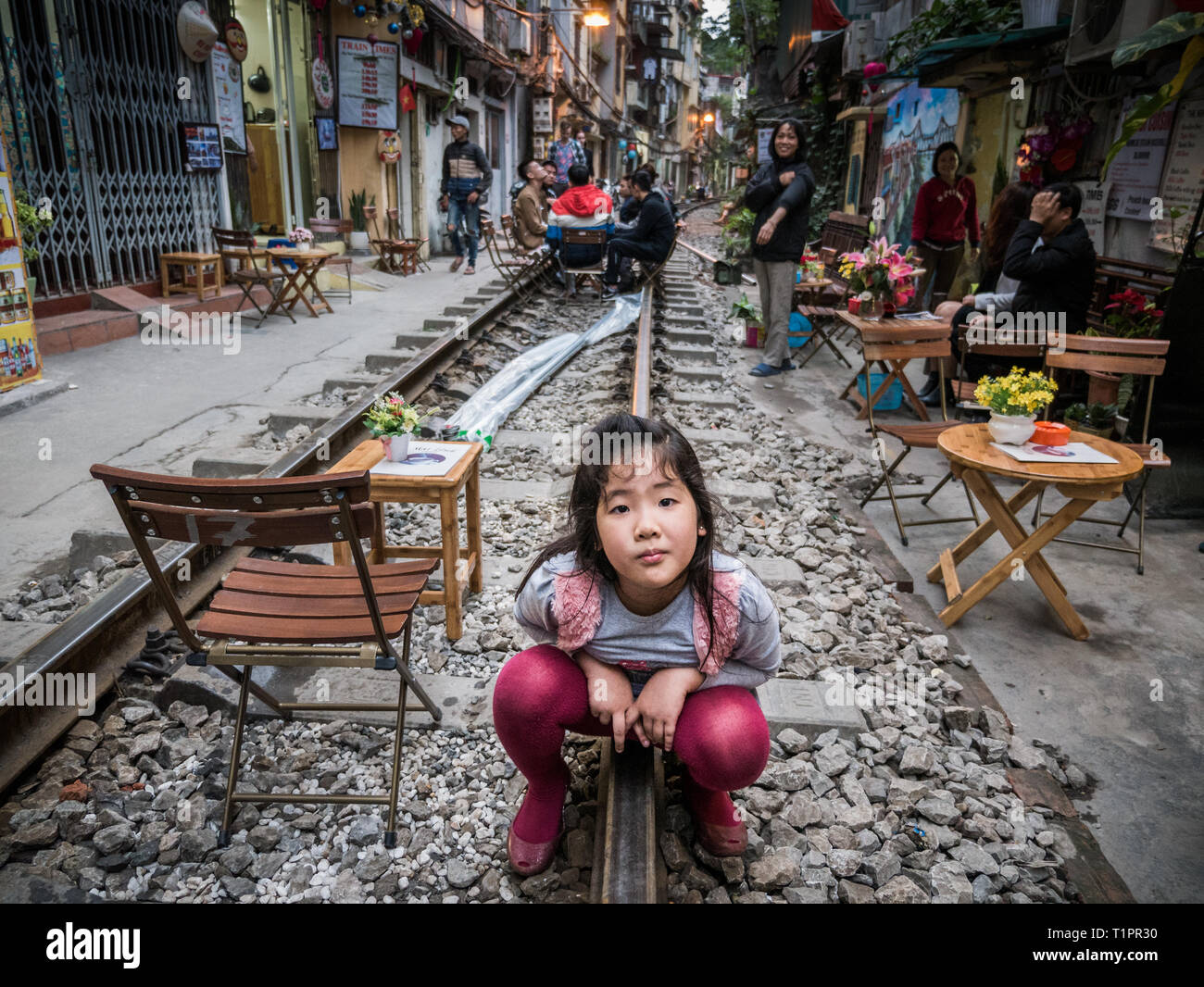 Neugierig vietnamesisches Mädchen hocken auf Schienen und sieht in die Kamera in Zug Straße der Stadt Hanoi, Vietnam Stockfoto