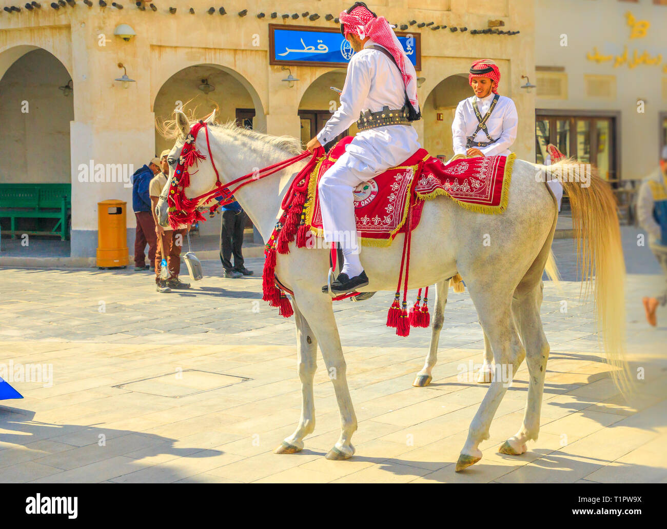 Doha, Katar - Februar 20, 2019: Nahaufnahme von Polizei am Pferd in traditioneller Kleidung bei Souq Waqif reiten Weiße arabische Pferde. Beliebte touristische Stockfoto