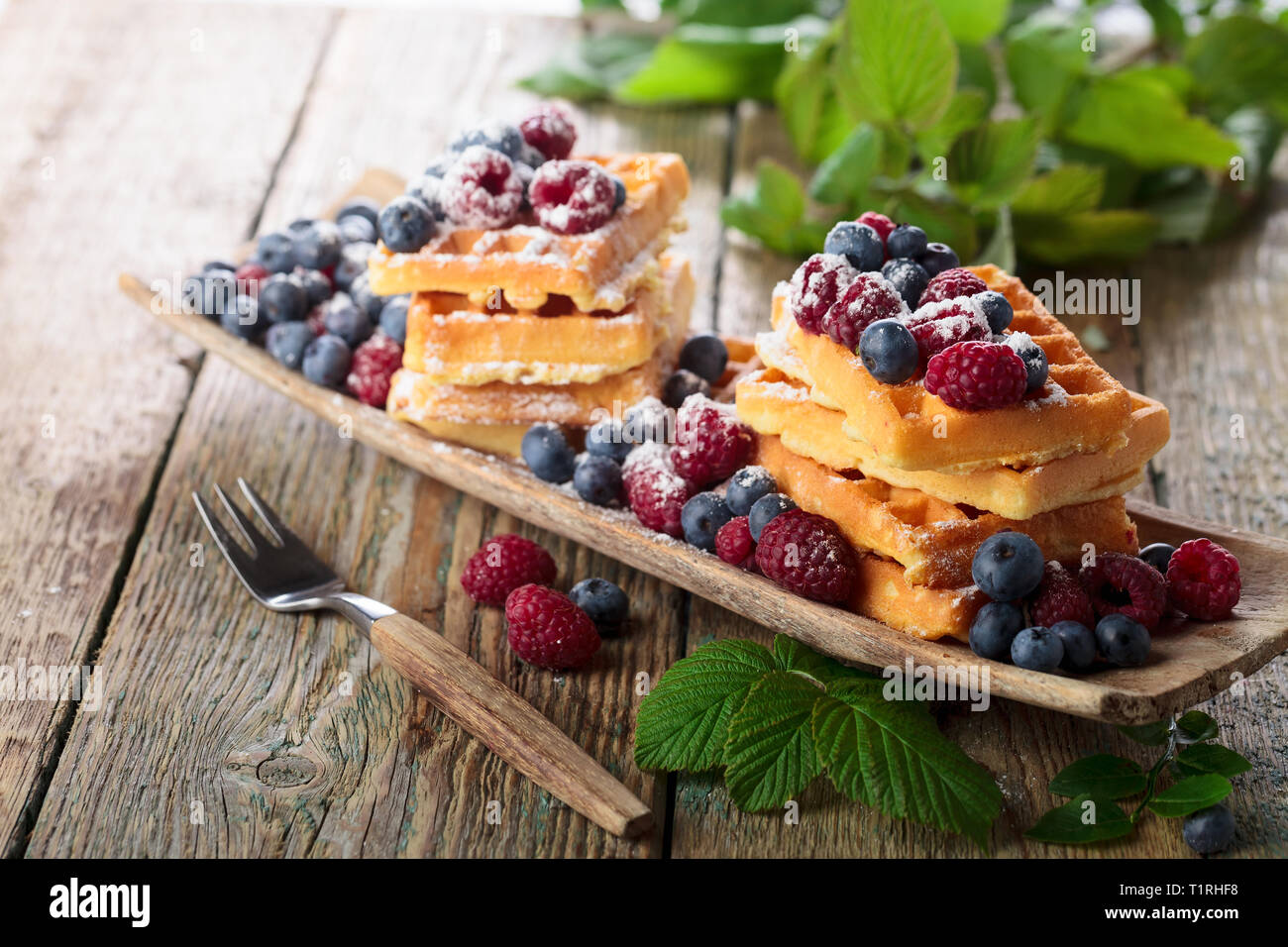 Waffeln mit Himbeeren und Blaubeeren auf einem alten Holztisch. Stockfoto