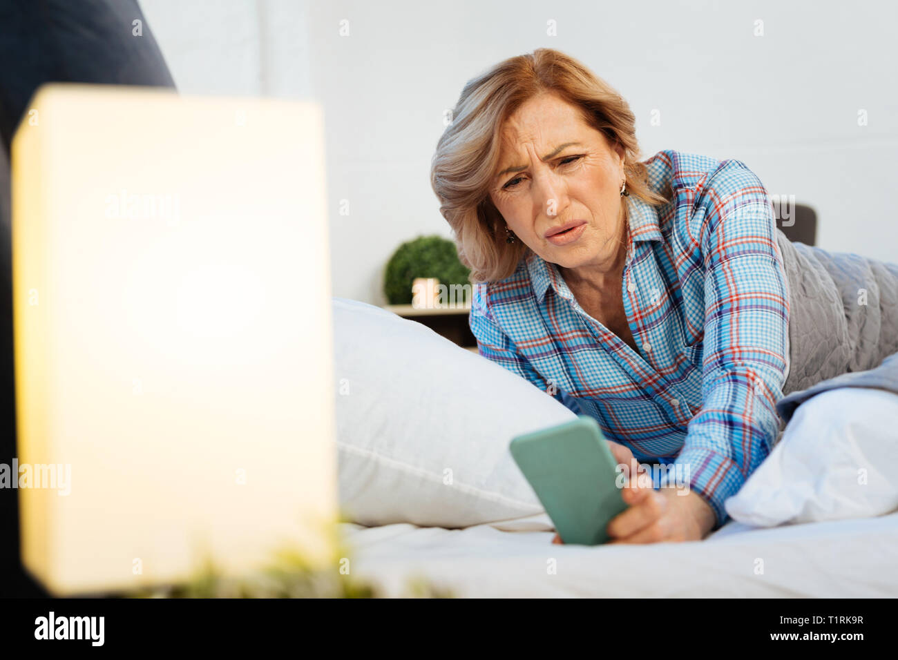 Verwirrt kurzhaarige erwachsenen Frau im hellen Pyjama suchen auf dem Bildschirm Stockfoto