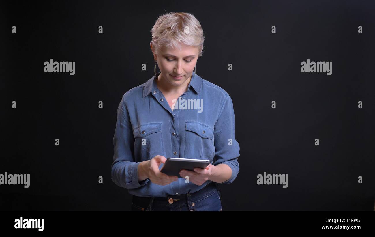 Closeup Portrait von Erwachsenen ziemlich kaukasischen Frauen mit kurzen blonden Haaren die Verwendung des Tablet vor der Kamera mit Hintergrund auf Schwarz Stockfoto