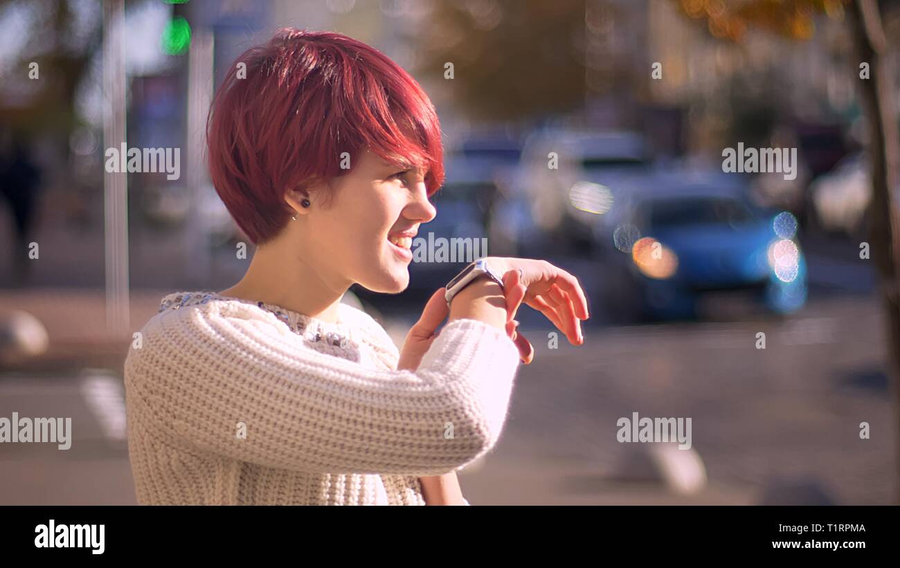 Porträt der jungen kaukasischen Rosa - behaarte mädchen freudig sprechen mit ihren Uhren auf sonnigen Stadt Hintergrund. Stockfoto