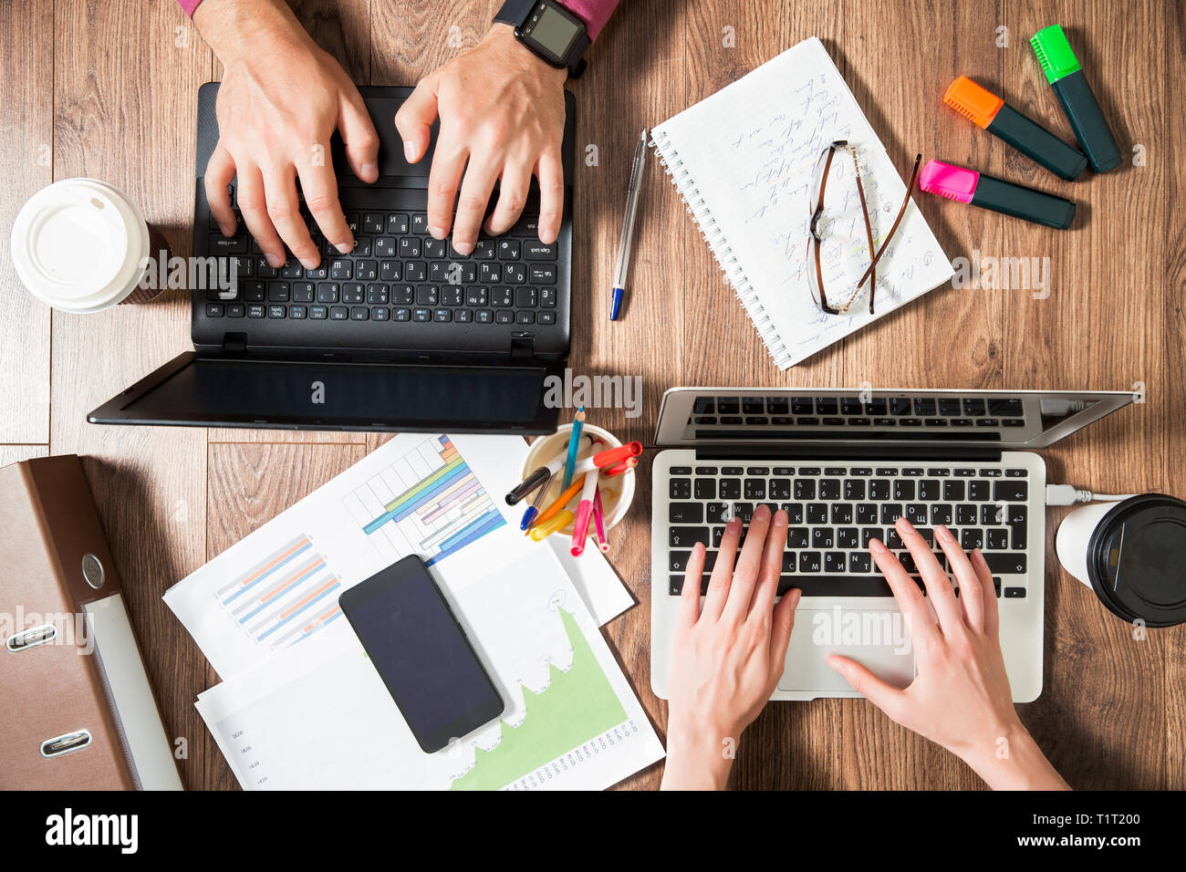 Zwei Personen im Büro Schreibtisch arbeiten, schreiben und mit Laptop, Ansicht von oben, flach. Smart Watch an Hand und Smart Phone auf dem Tisch. Kaffeetasse Stockfoto