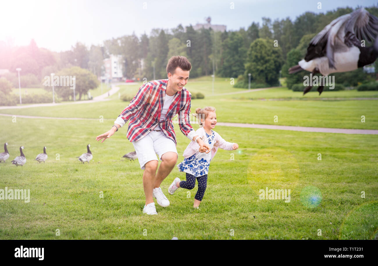 Vater und Tochter Spaß im Sommer Tag. Kanadische Gänse jagen, die auf die Wiese und Lachen. Gesunde Lebensweise. Helsinki, Finnland Stockfoto