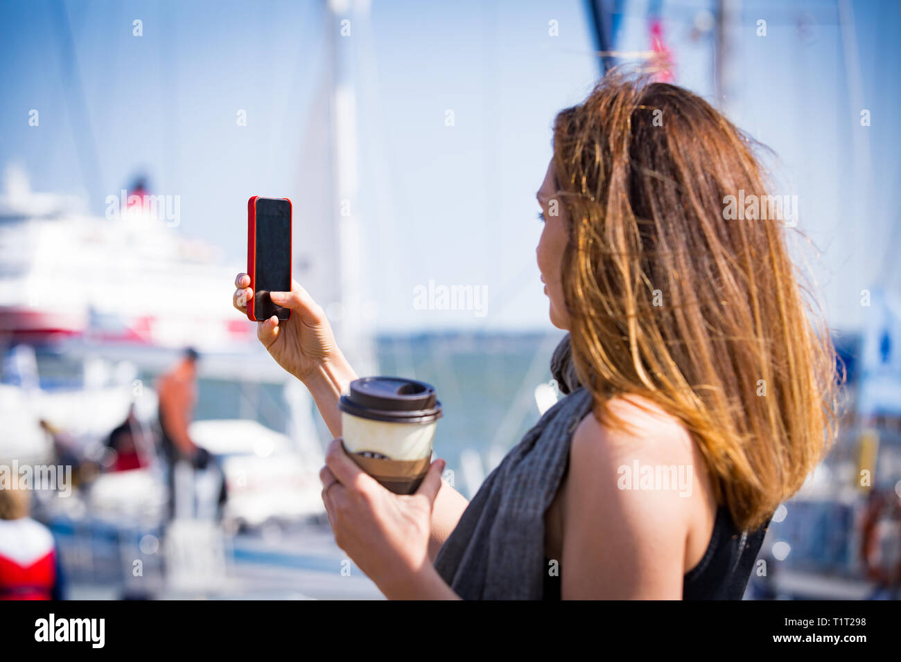 Schöne Frau mit Foto mit Smart Phone. Bild von Hafen mit Segelbooten, am Meer. Sonnigen Sommer bucht. Die selfie und Kaffee zu trinken. Stockfoto