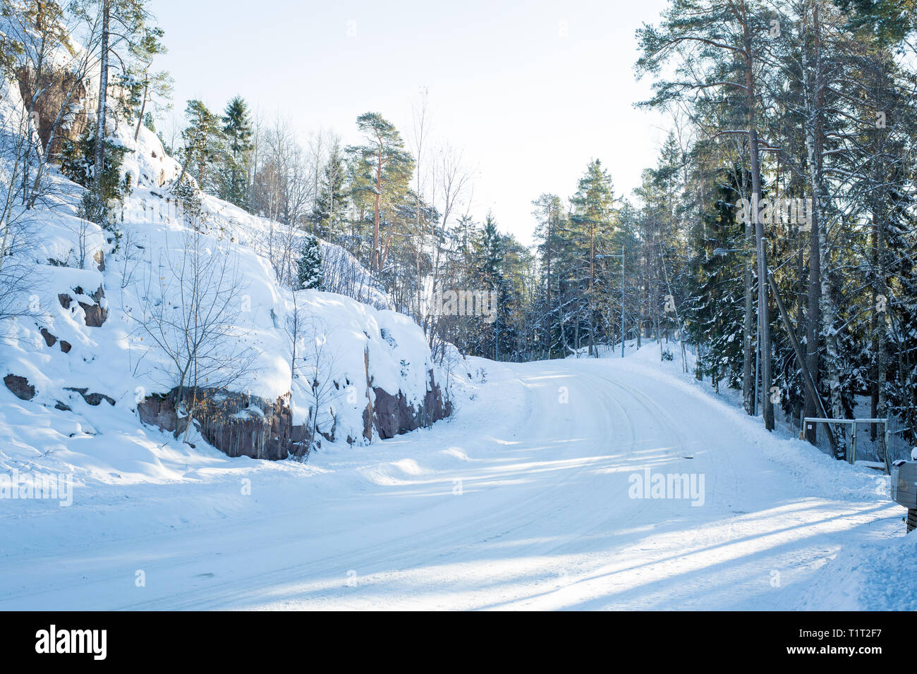 Finnland. Uusima. Schnee Land straße Drehen im Winter. Landschaft mit Wald, Felsen, Sonne auf den Bäumen. Stockfoto