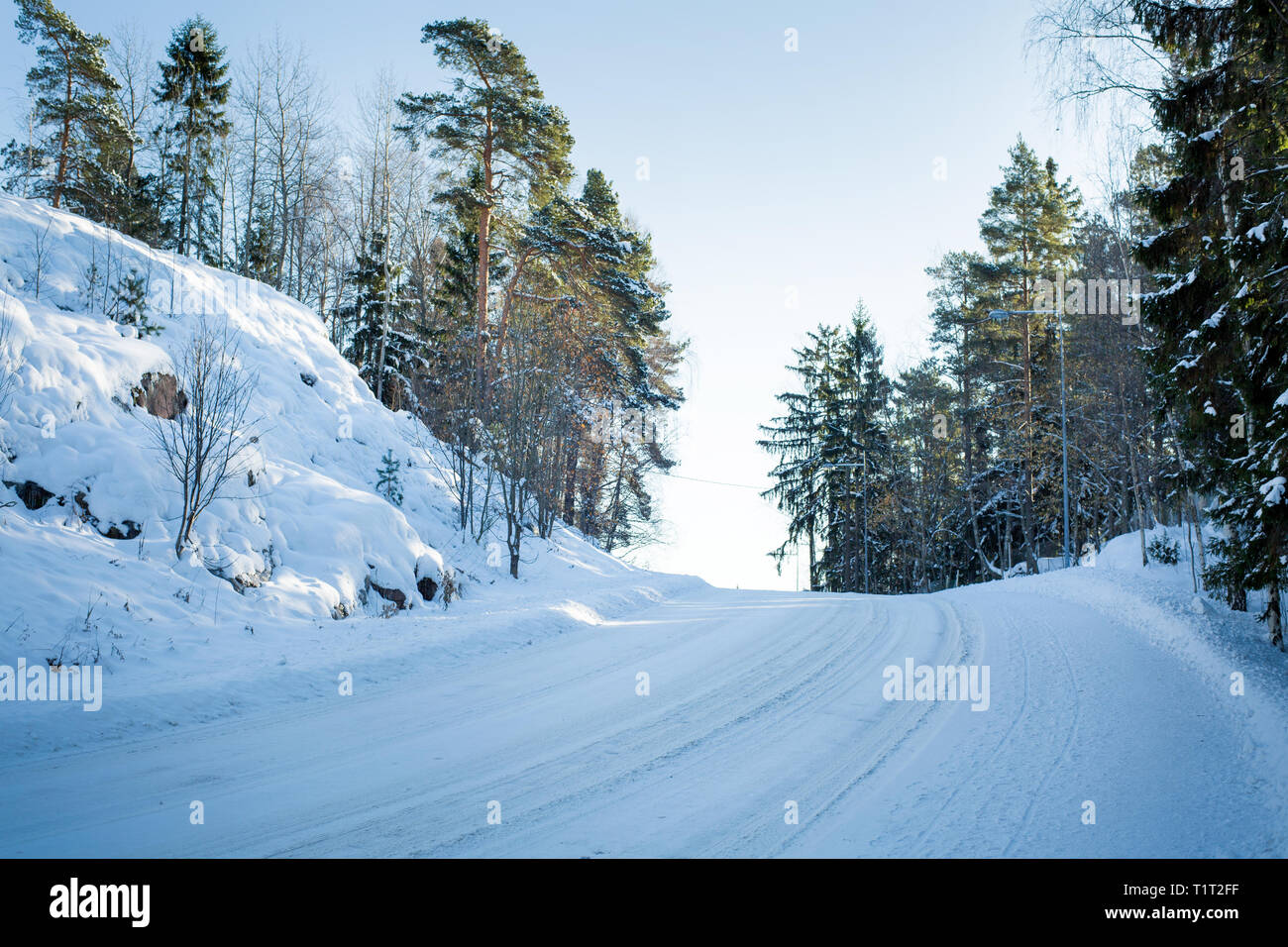 Finnland. Uusima. Schnee Land straße Drehen im Winter. Landschaft mit Wald, Felsen, Sonne auf den Bäumen. Stockfoto