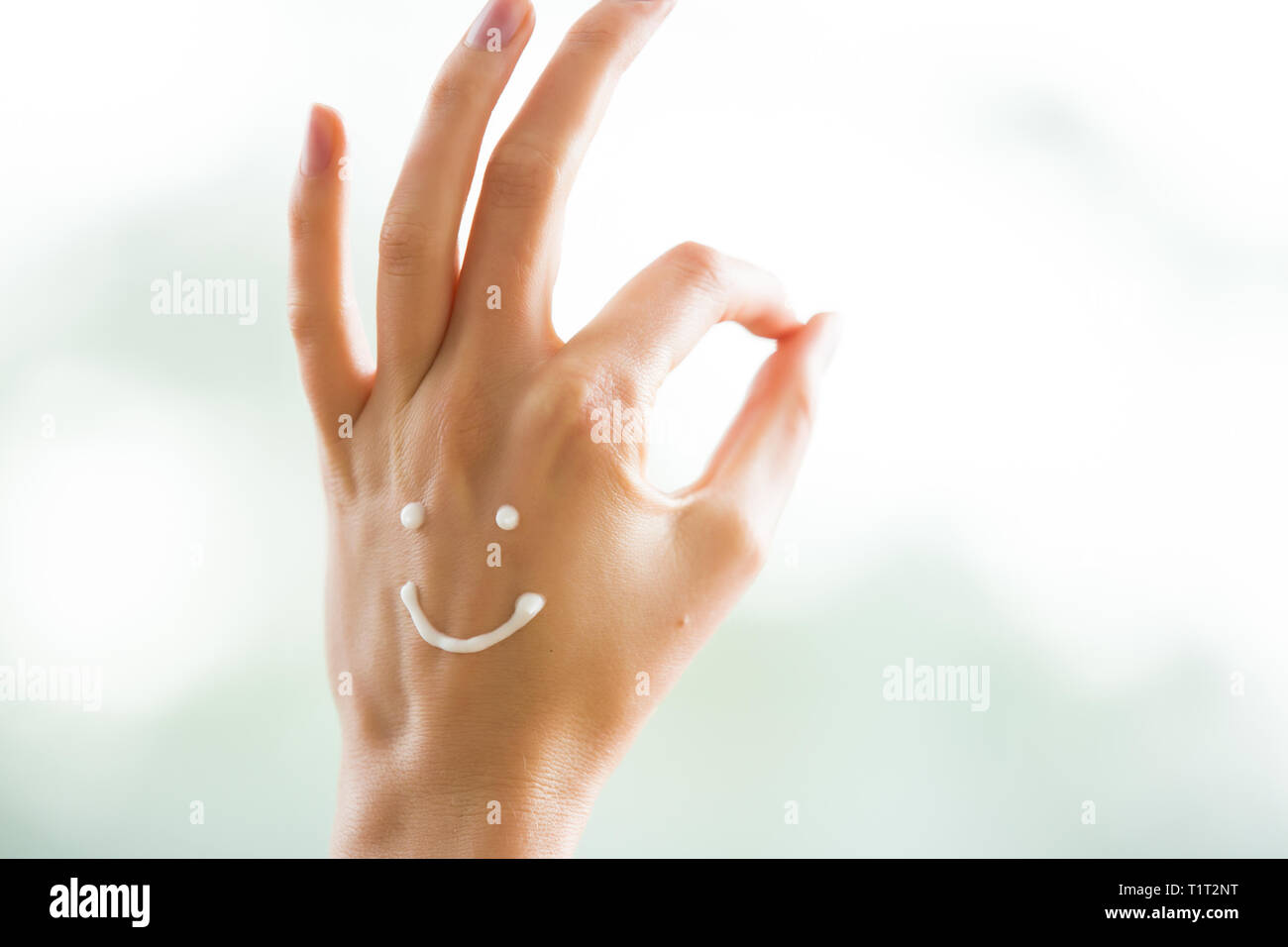 Closeup Frau schöne Hände mit langen Fingern, die feuchtigkeitsspendende und beruhigende Creme auf der Haut. Lustige lächelnde Gesichter, emoji. Ok anmelden. Stockfoto
