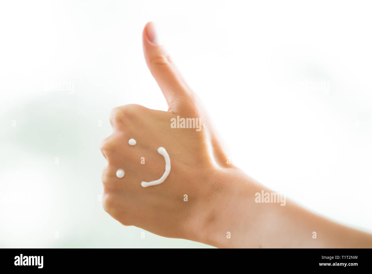 Closeup Frau schöne Hände mit langen Fingern, die feuchtigkeitsspendende und beruhigende Creme auf der Haut. Lustige lächelnde Gesichter, emoji. Daumen hoch. Stockfoto