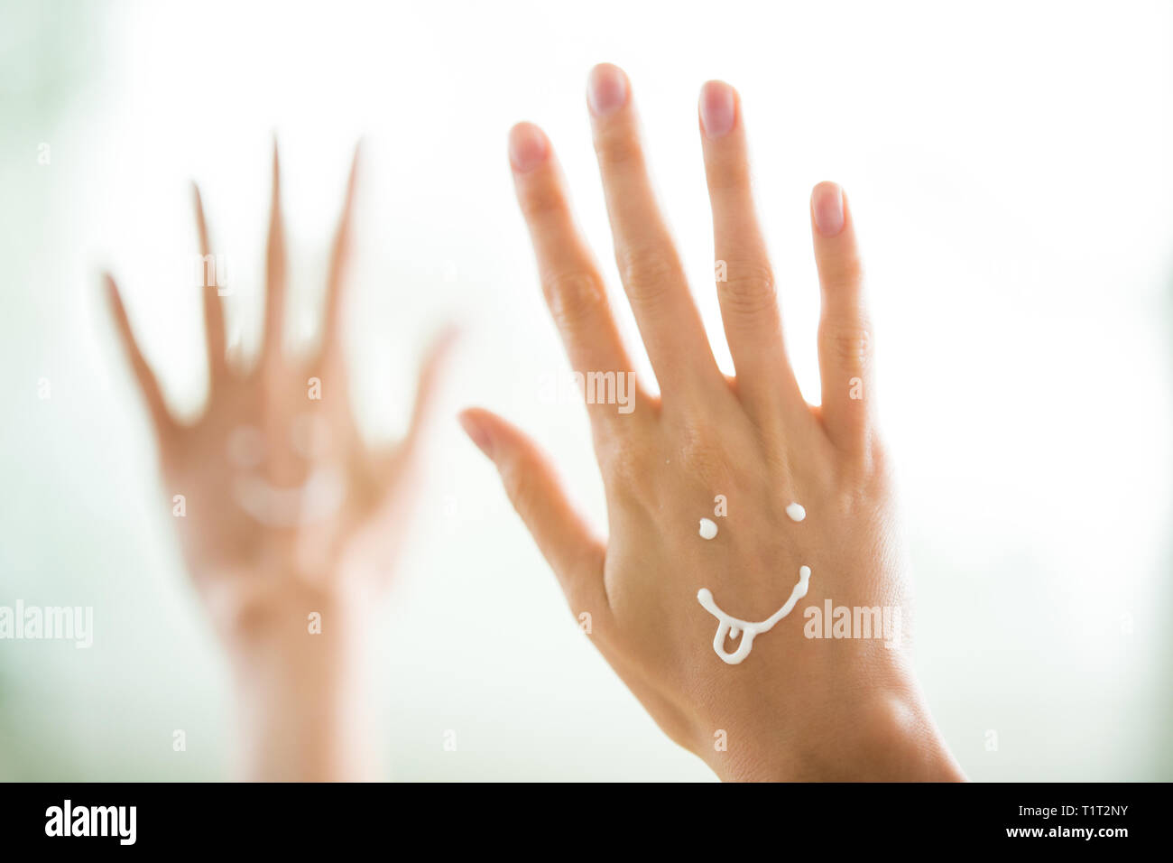 Closeup Frau schöne Hände mit langen Fingern, die feuchtigkeitsspendende und beruhigende Creme auf der Haut. Lustige lächelnde Gesichter, emoji. Stockfoto