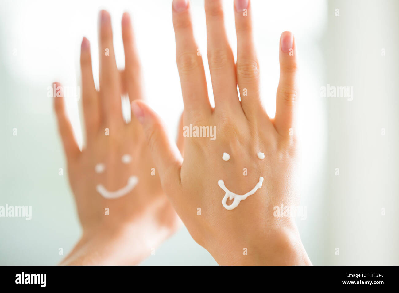 Closeup Frau schöne Hände mit langen Fingern, die feuchtigkeitsspendende und beruhigende Creme auf der Haut. Lustige lächelnde Gesichter, emoji. Stockfoto