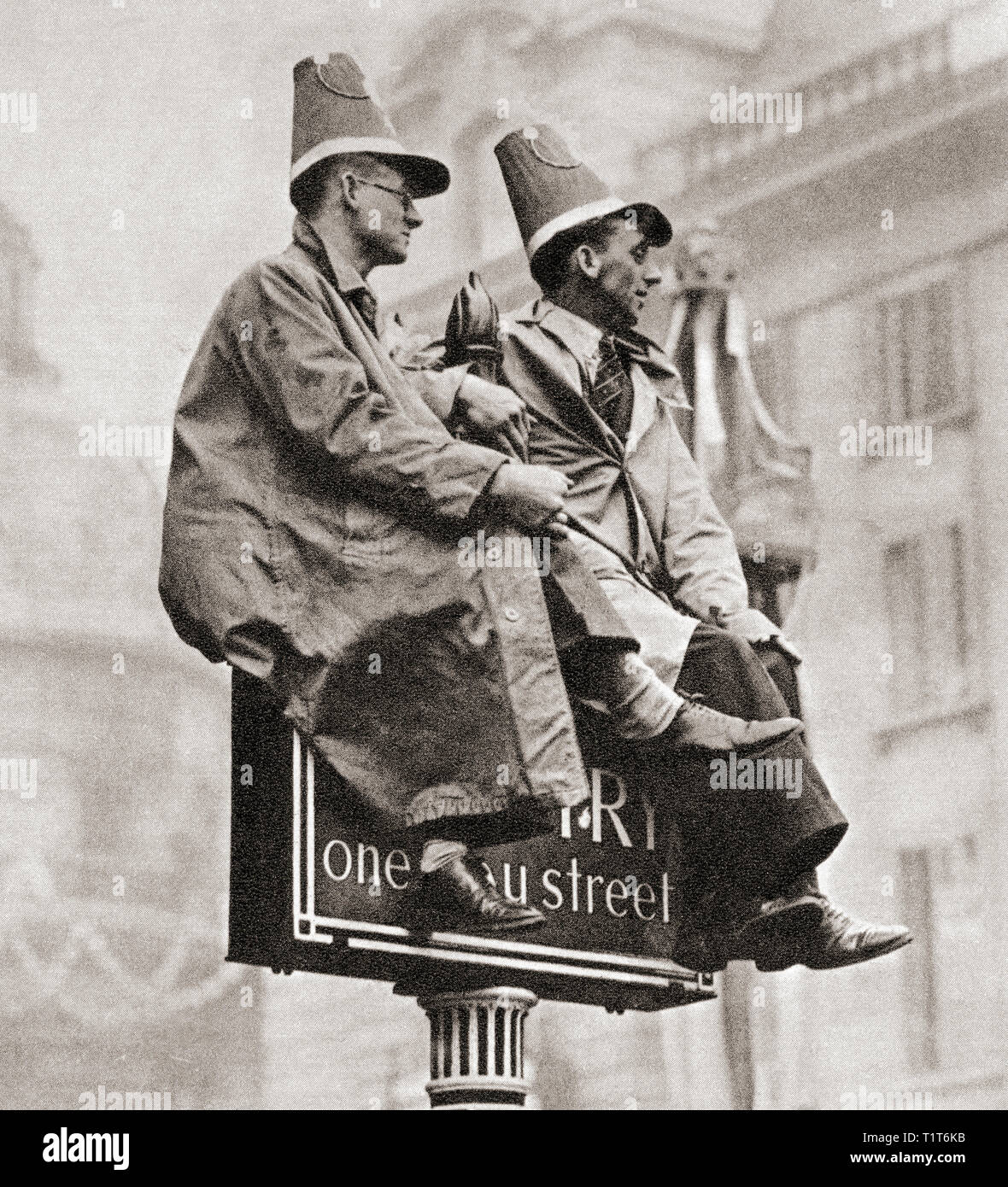Zwei Männer auf einem Verkehrsschild, um eine bessere Ansicht der Krönungsprozession von George VI und Königin Elizabeth, London, England, 1937 zu erhalten. Von der Krönung in Bilder, veröffentlicht 1937. Stockfoto