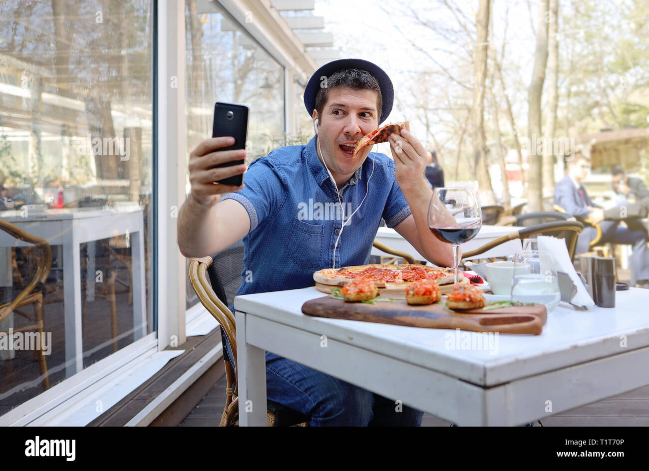 Stattliche hunger Mann essen Pizza und zeigt in einer Videokonferenz mit seinen Freunden. Reisende im Ausland und Roaming Konzept. Stockfoto