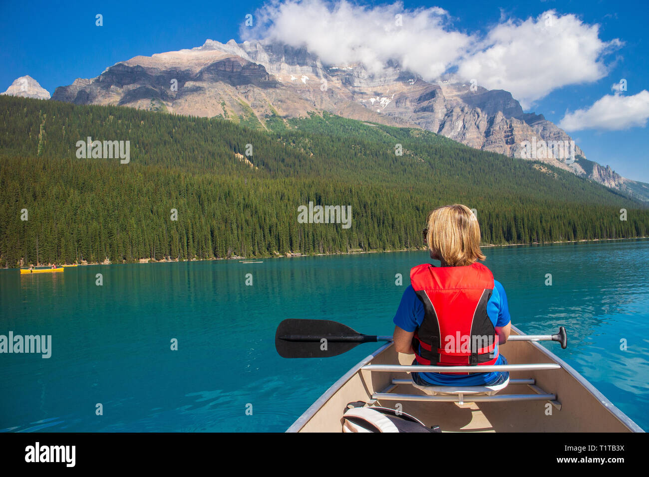 Frau Bootfahren in einem Kanu auf Moraine Lake, Kanada mit Bergen im Hintergrund Stockfoto