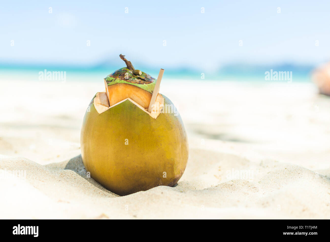 Frische junge Kokosnuss liegen auf dem Sand strand Hintergrund mit Stroh fertig zum Trinken. Urlaub in den Tropen Travel Concept Stockfoto