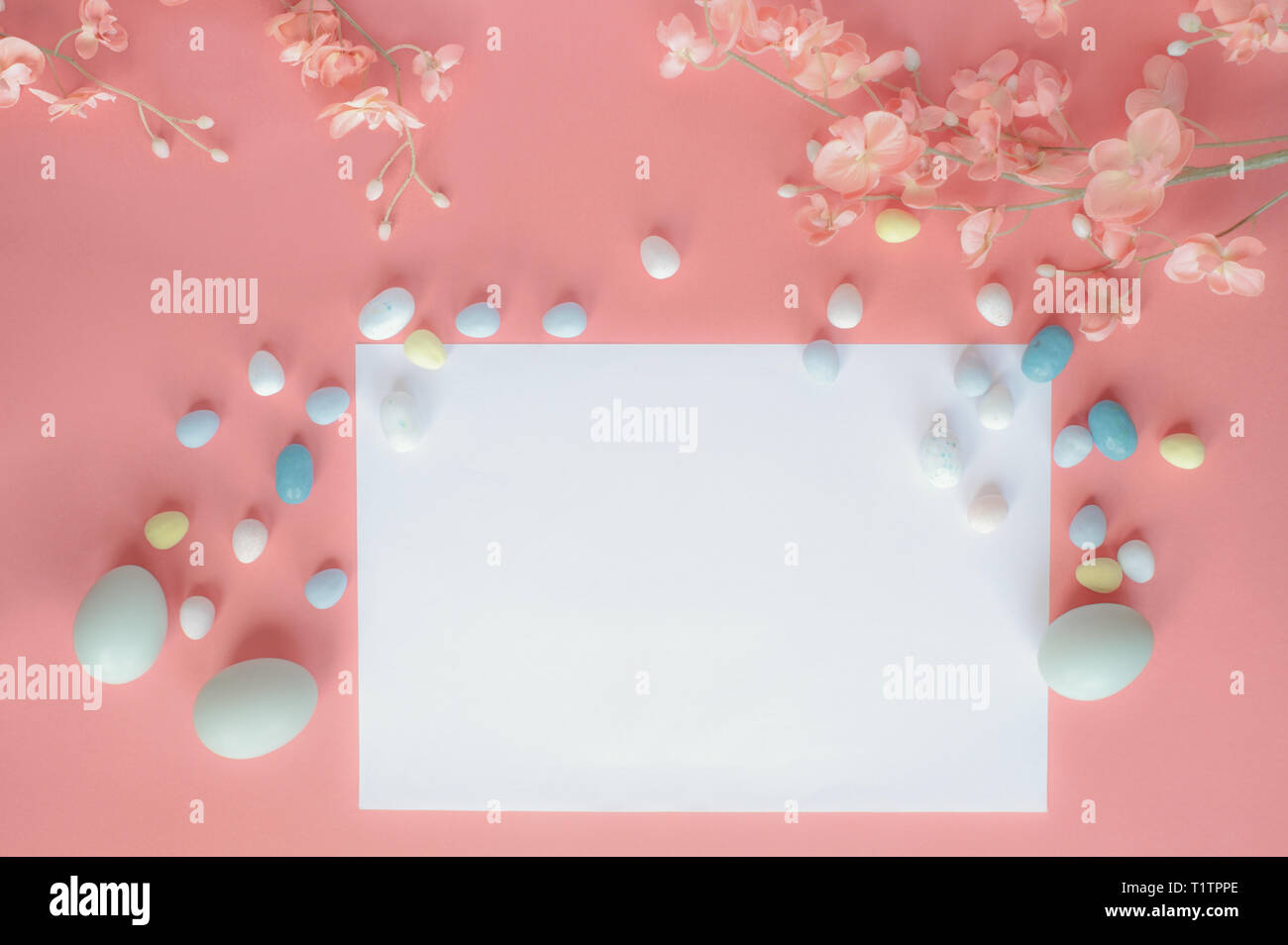 Pastell Ostereier, Malz Bonbon, Schokolade, Eier, und Blüten über einen Coral farbigen Hintergrund mit einer leeren Karte zu kopieren. Stockfoto