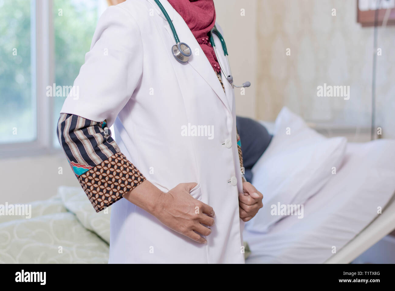 Körper Teil der weiblichen Hijab muslimischen Arztes Posieren vor der Kamera mit ihrer Frau, Patient liegt auf dem Bett hinter ihr im Krankenhaus Zimmer Stockfoto