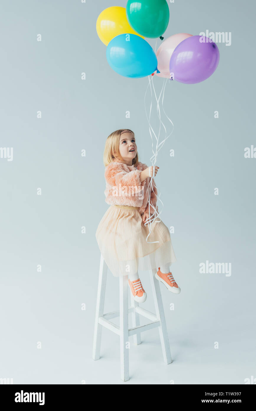 Cute kid in Fellimitat Mantel und Rock sitzt auf Hochstuhl und Holding Ballons Stockfoto