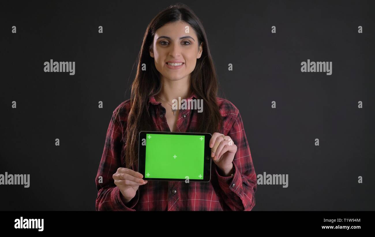 Porträt der jungen langhaarigen Mädchen in plaided Shirt demonstrieren horizontalen grünen Bildschirm des Tablet auf schwarzem Hintergrund. Stockfoto