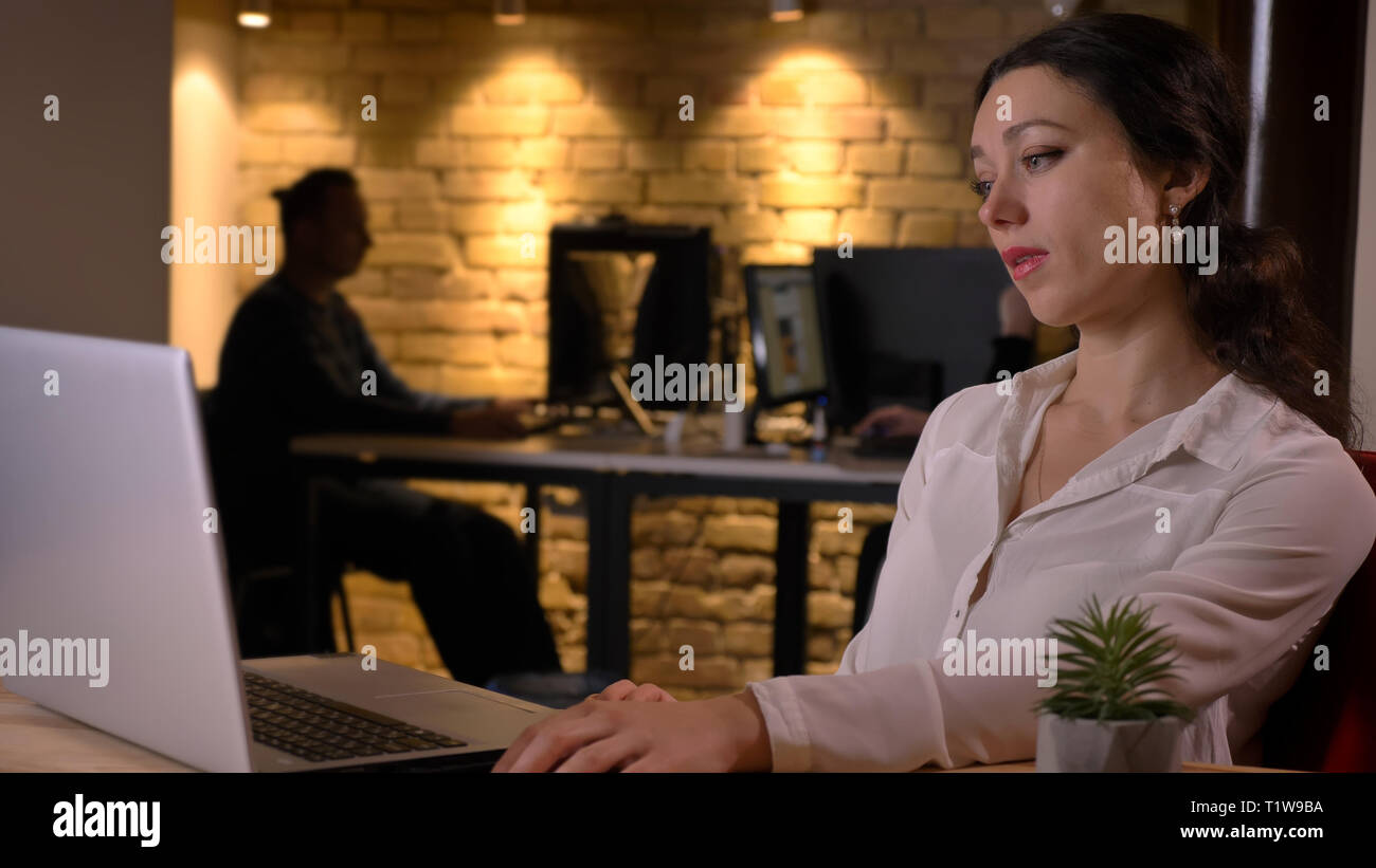 Closeup Shooting für junge gelangweilt kaukasischen Geschäftsfrau Tippen auf dem Laptop und ineffiziente drinnen am Arbeitsplatz Stockfoto