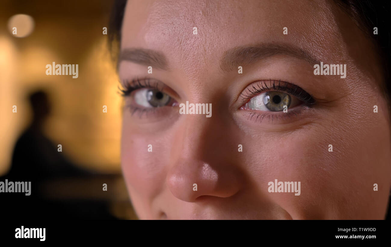 Closeup Portrait von jungen Hübschen kaukasischen Frauen Gesicht mit Augen geradeaus auf Kamera mit fröhlichen Gesichtsausdruck im Innenbereich Stockfoto