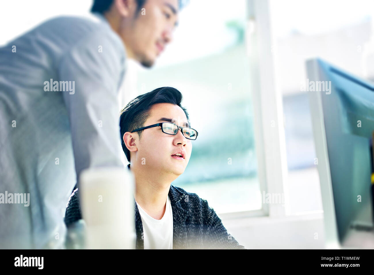 Zwei junge asiatische Geschäftsleute in einer Diskussion vor der Desktop-Computer im Büro. Stockfoto