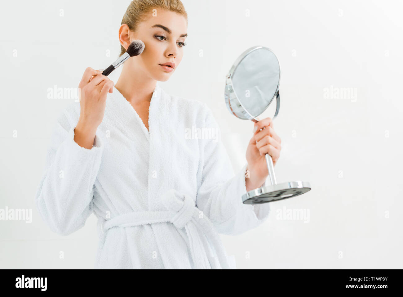 Attraktive, blonde Frau in weißen Bademantel mit kosmetischen Bürste und Spiegel Stockfoto