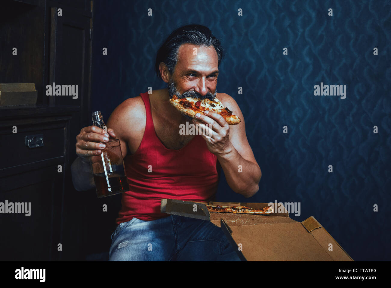 Brutale bärtiger Mann zu Hause essen Pizza und trinken Alkohol. Stockfoto