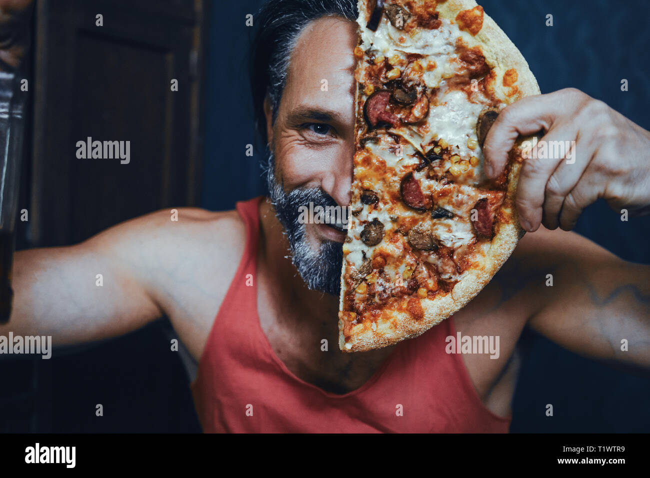 Brutale bärtiger Mann zu Hause essen Pizza und trinken Alkohol. Stockfoto