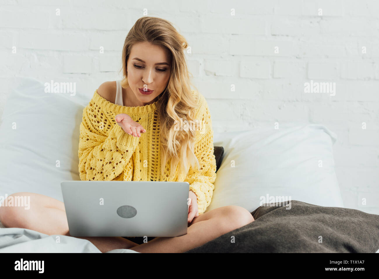 Schöne Mädchen im Bett sitzen, mit Laptop und Blasluft küssen, während in Video Anruf zu Hause Stockfoto