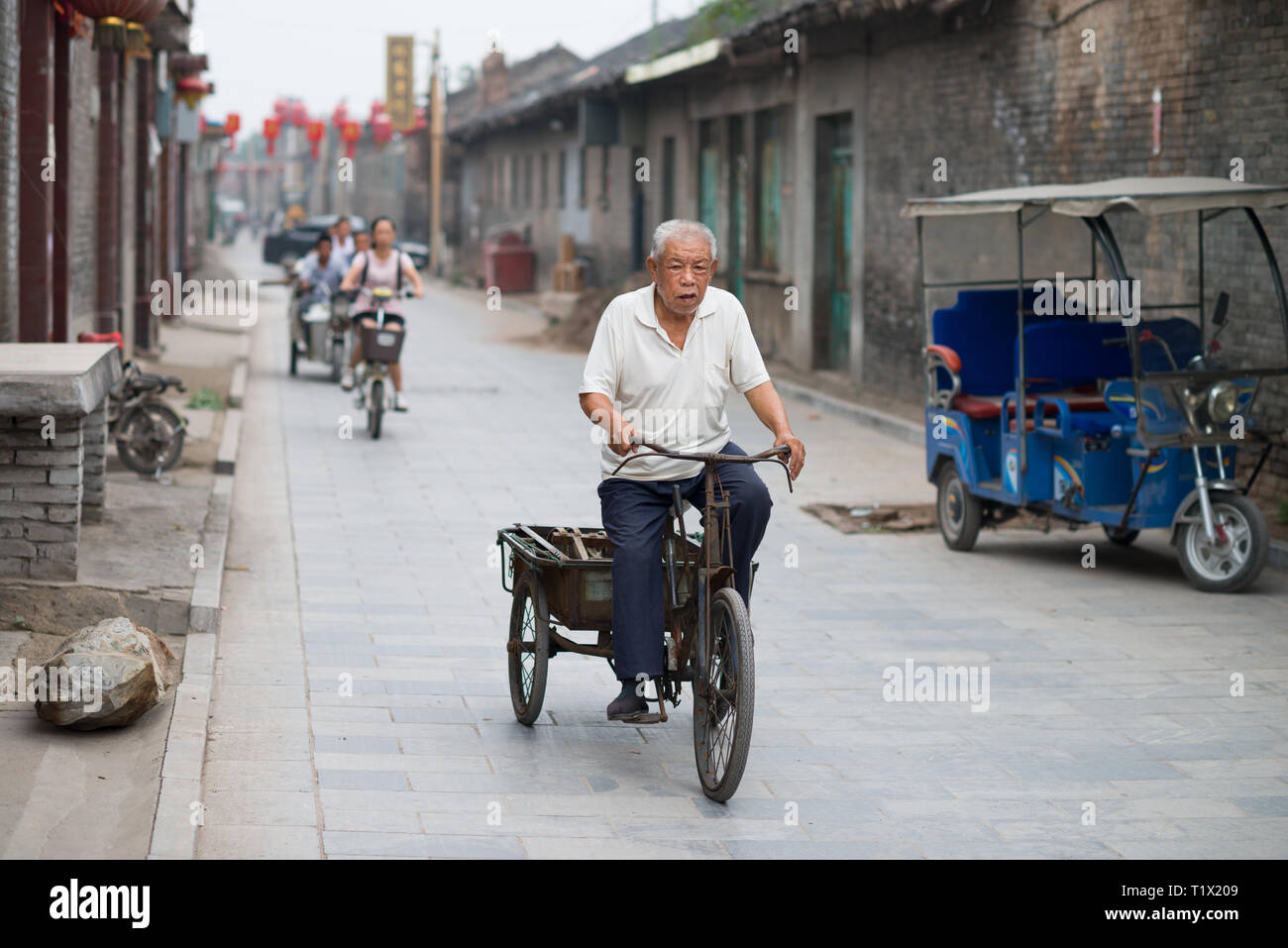 Pingyao, China - 08 14 2016: Ein älterer auf ein Dreirad in einer Straße von Pingyao, Shanxi, China Stockfoto
