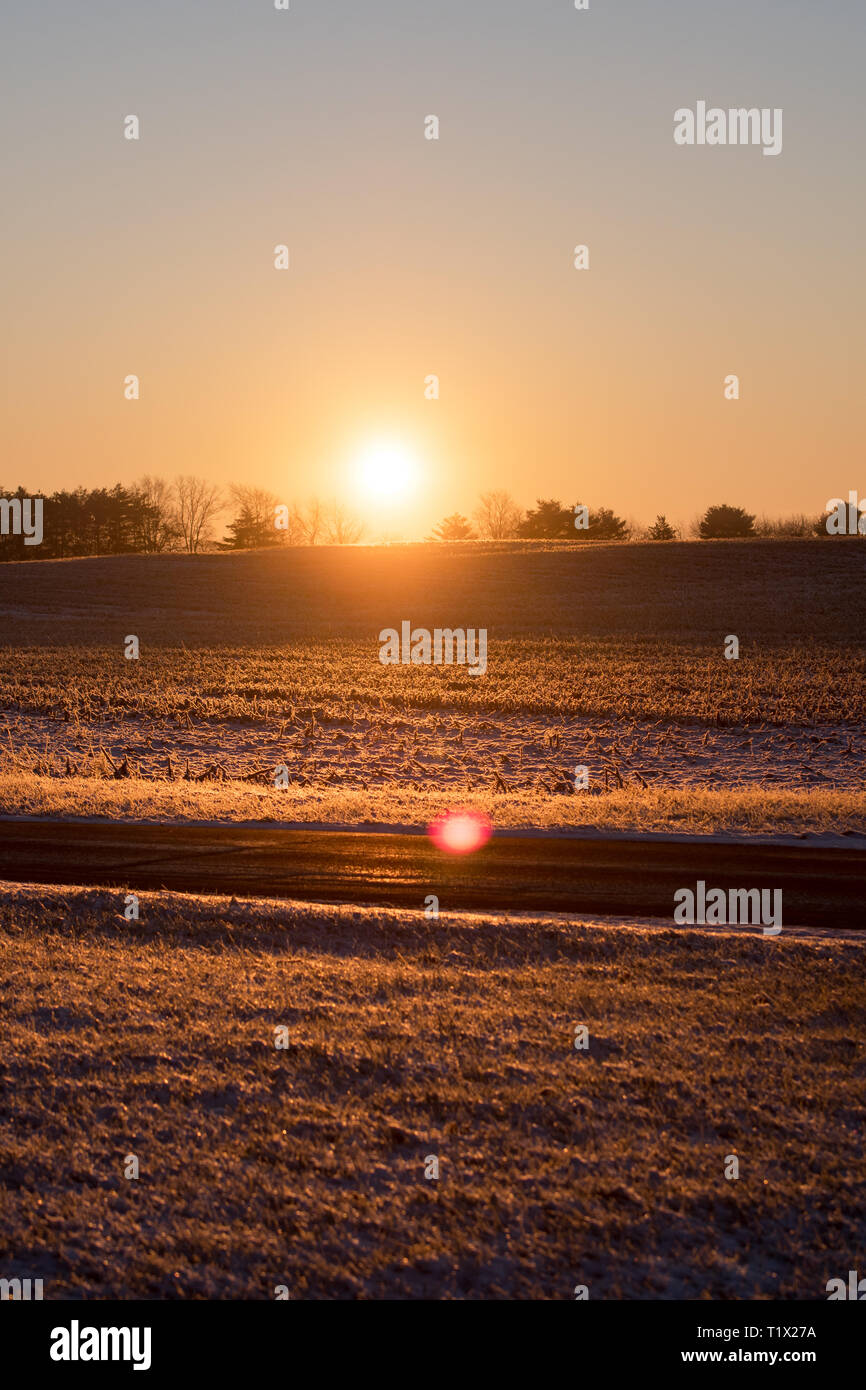 Ein tief orange Sonnenaufgang durch ein Feld und über eine Straße, glänzend Stockfoto