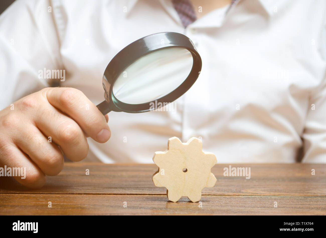 Geschäftsmann untersucht eine Holz- gang durch ein Vergrößerungsglas. Untersuchung und Analyse der Geschäftsprozesse und der Themen. Eine Zahnradbahn von einem big business Machin Stockfoto