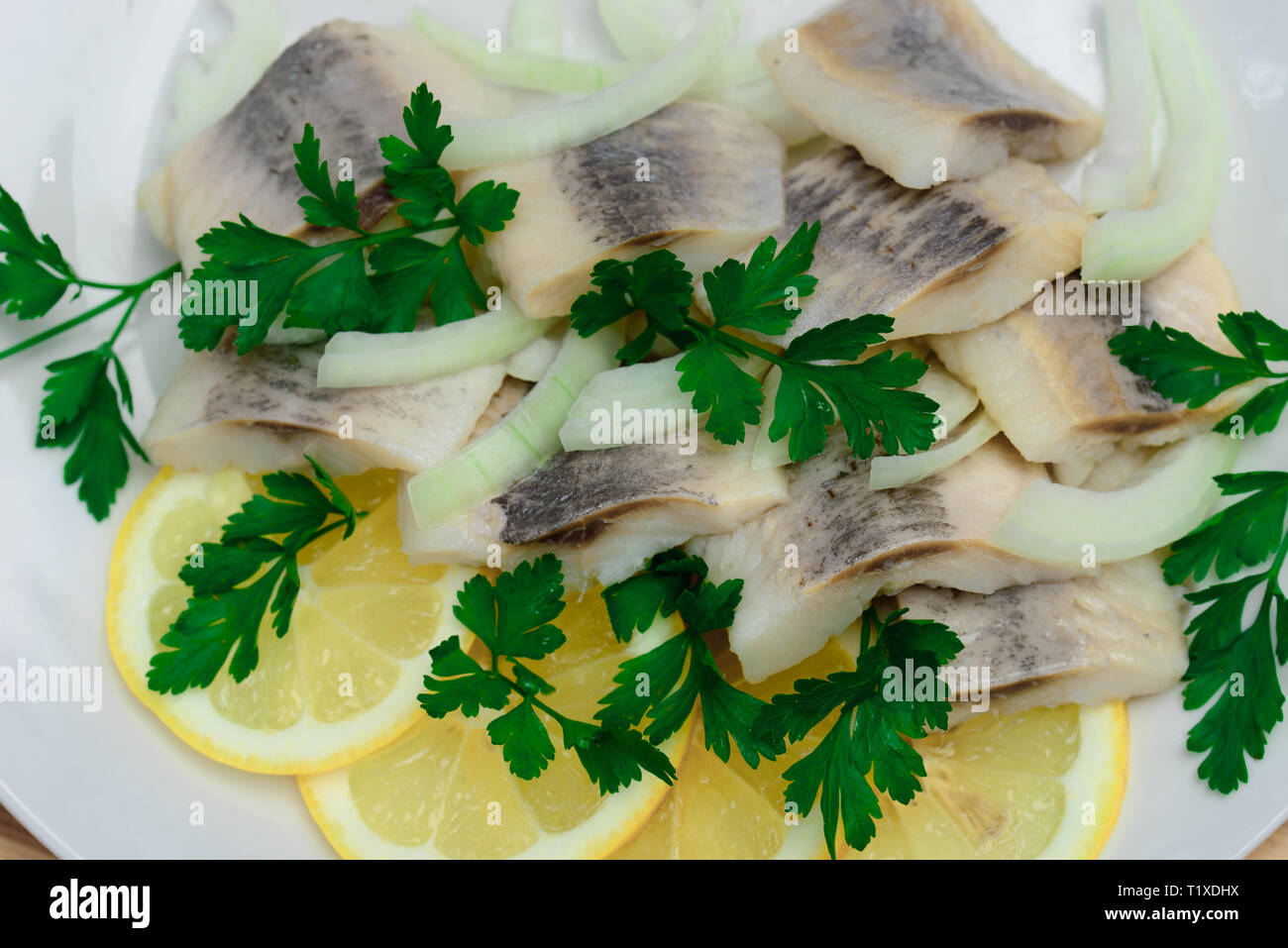 Marimated Hering mit Petersilie, Zwiebel und Zitronenscheiben auf weiße Platte Stockfoto