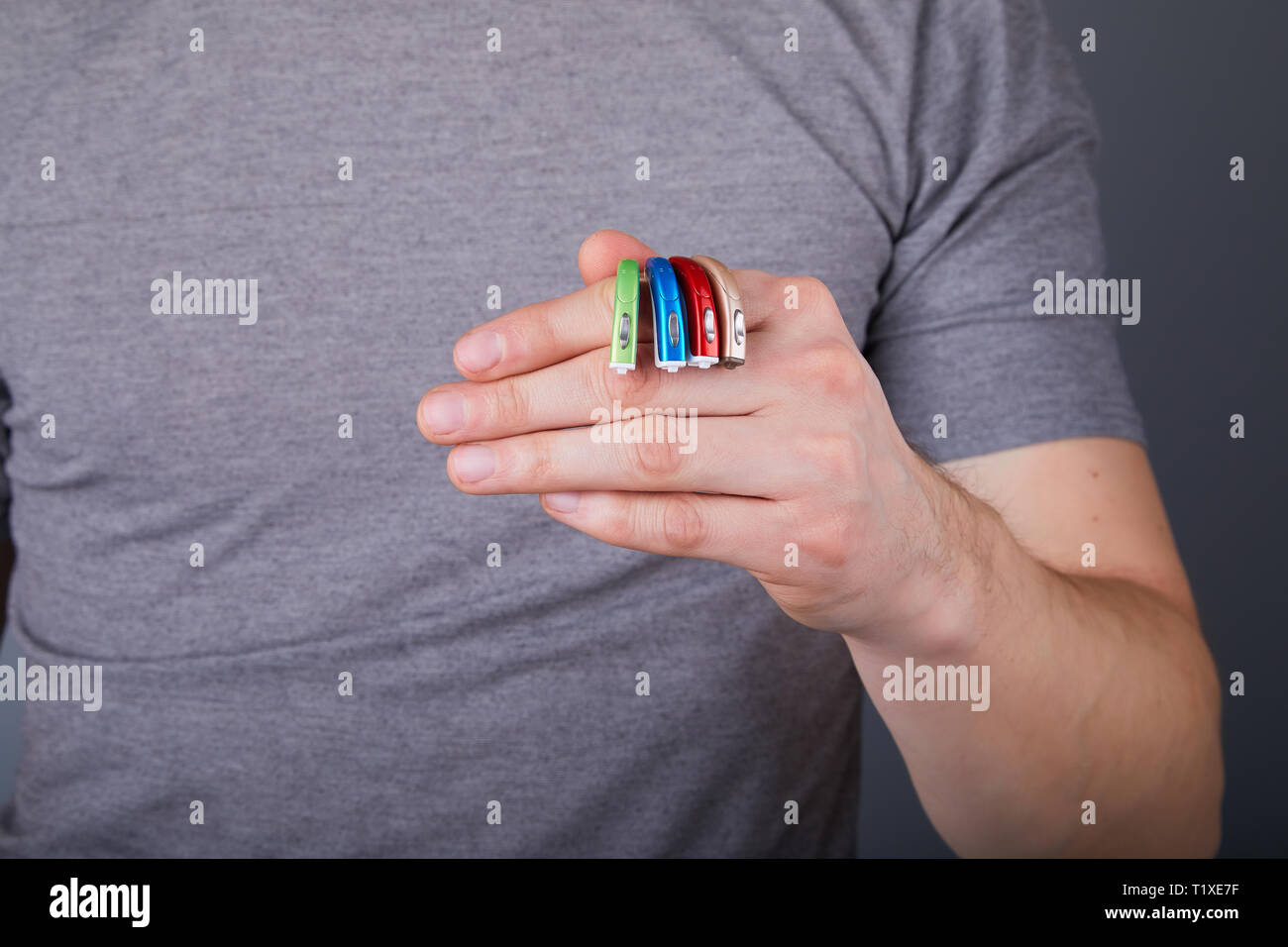Mann mit Hörgeräten der verschiedenen Farben, Nahaufnahme. Hörgeräte auf grauem Hintergrund, Alternative zur Chirurgie. Stockfoto