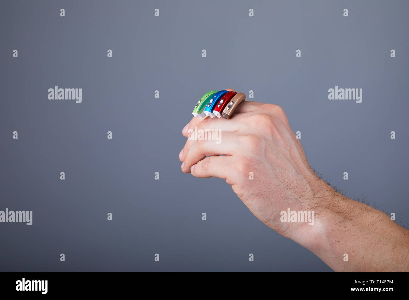 Mann mit Hörgeräten der verschiedenen Farben, Nahaufnahme. Hörgeräte auf grauem Hintergrund, Alternative zur Chirurgie. Stockfoto