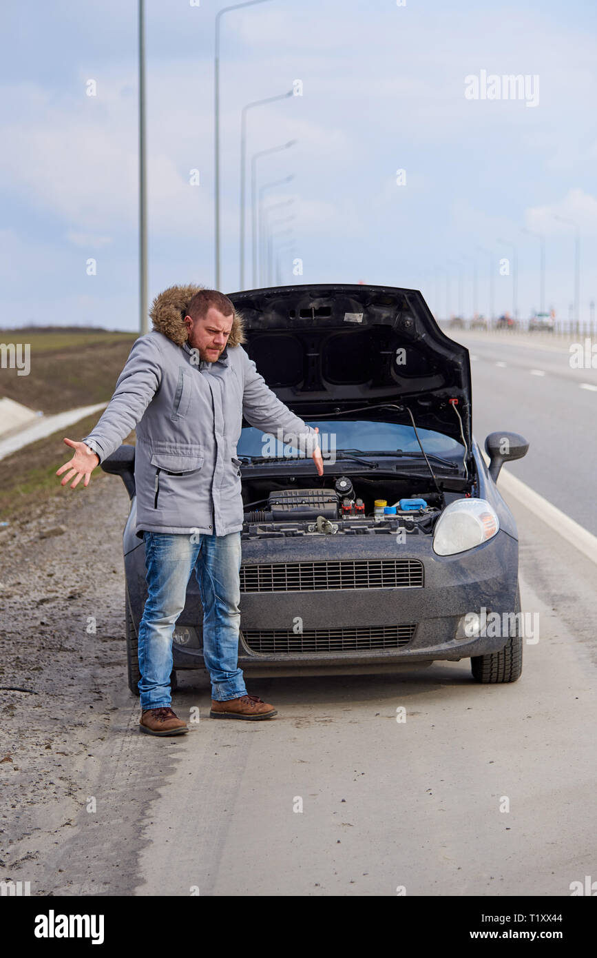 Verzweifelten jungen Mann mit einem kaputten Auto auf der Autobahn. Stockfoto