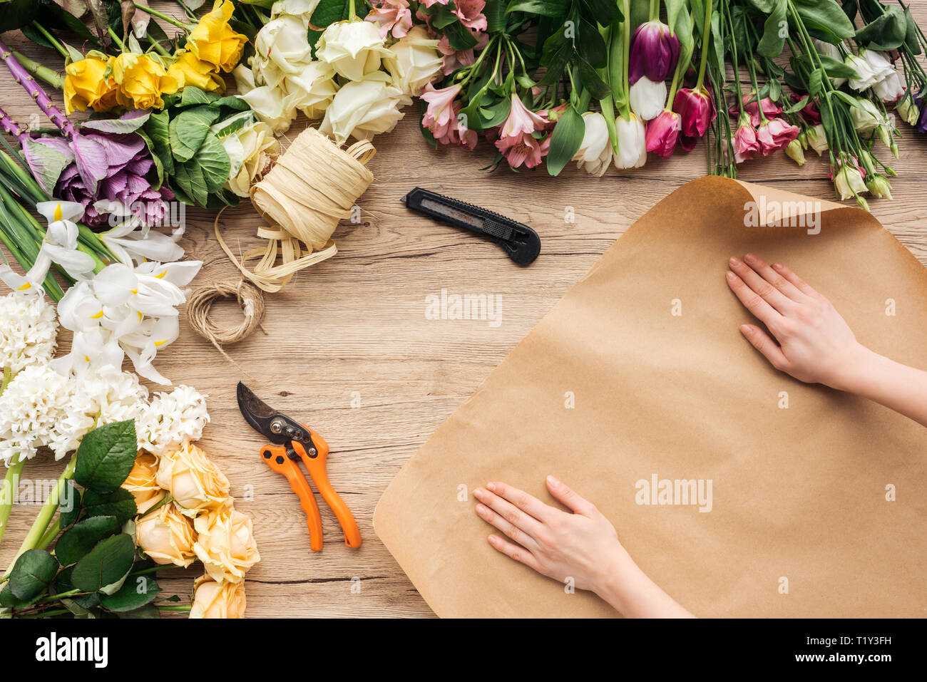7/8-Ansicht von Floristen mit Handwerk Papier und bunte Blumen auf Holz- Oberfläche Stockfoto