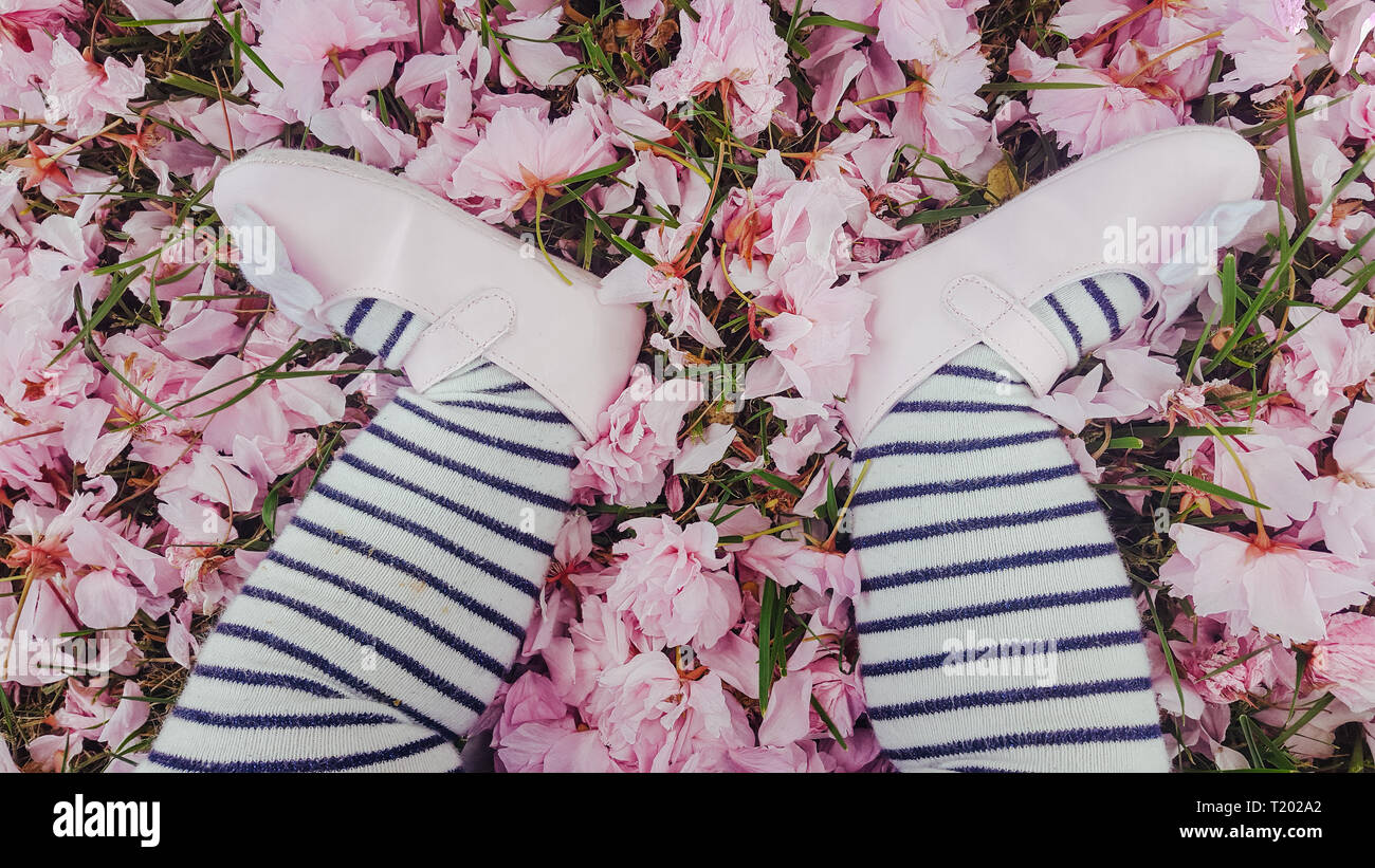 Kleinkind Mädchen im Gras in rosa Blütenblätter fallen, Gestreifte Strumpfhosen und rosa Schuhe Stockfoto