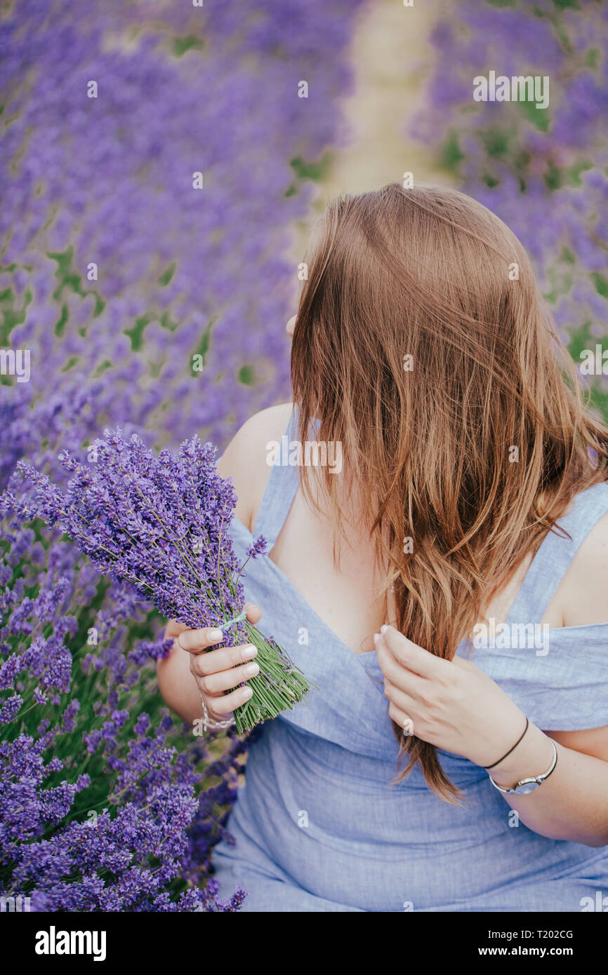 Plus Size curvy Frau mit langem Haar der Lavendel in Surrey, England, Mayfield. Fashion Outfit blaues Kleid, halten Strauß Blumen. Von der Seite. Stockfoto