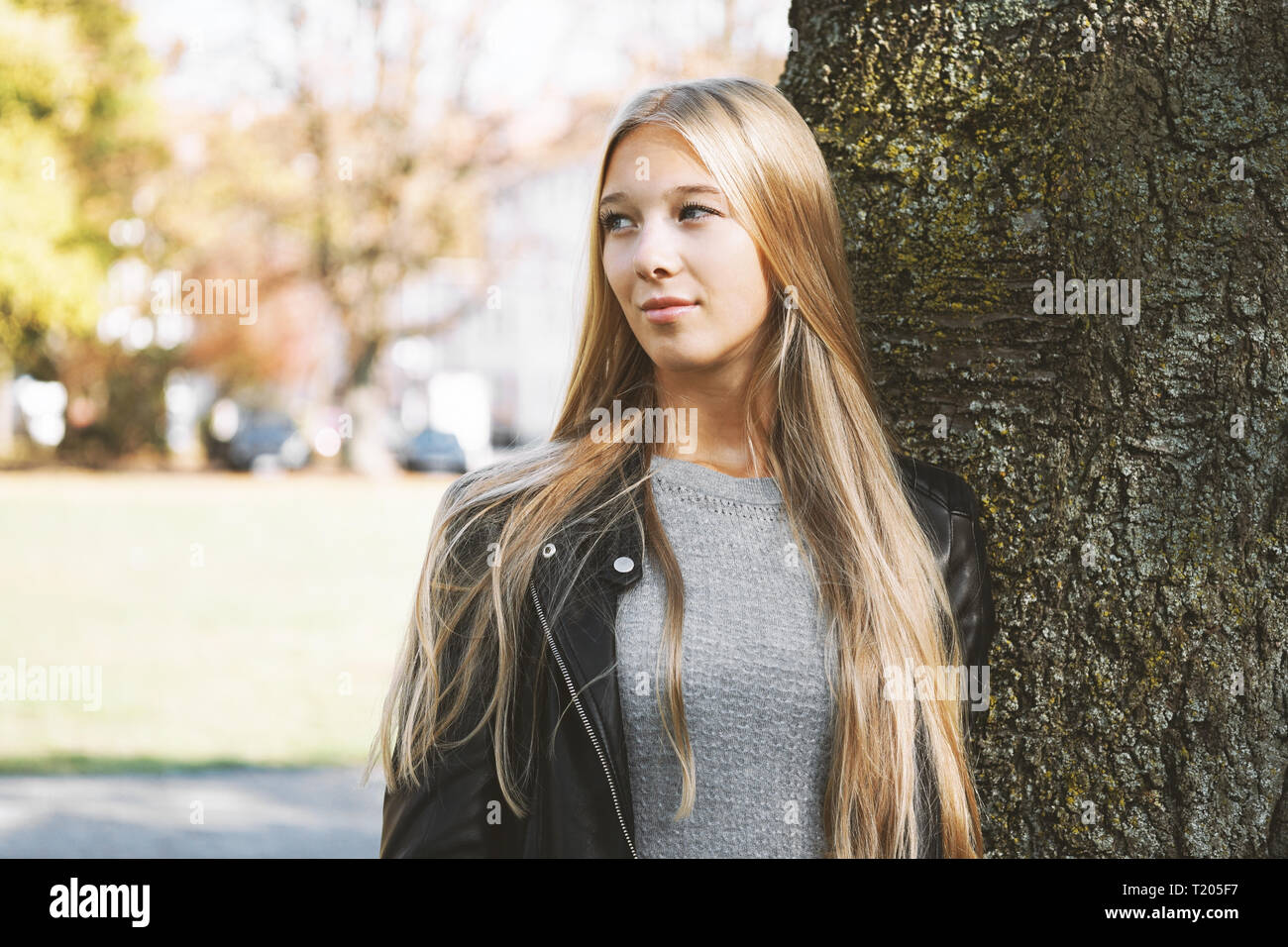 Verträumtes Teenager-Mädchen, das sich gegen den Baum lehnt Stockfoto